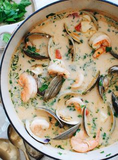 a white bowl filled with seafood and clam chowder next to silver spoons