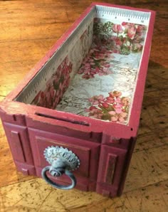 a pink box with flowers on it sitting on top of a wooden table next to a door knocker