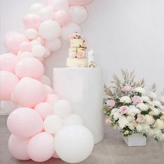 there is a cake on top of a table surrounded by pink and white balloons in the air