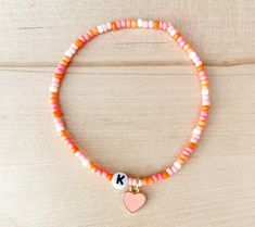 a beaded bracelet with a pink heart and k charm on it's end