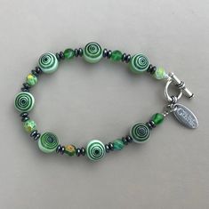 "This beautiful green Millefiori Glass and Hematite Bracelet is designed and made in Ireland. The toggle clasp is pewter. The bracelet is 8\" in length, is made on wire and has a toggle clasp. The bracelet can be made longer or shorter. There are also matching necklace options. Millefiori Glass is a type of mosaic glassware characterised by a flowerlike pattern. The term millefiori is a combination of the Italian words Mille meaning thousand and fiord meaning flowers." Green Nickel Free Bracelets With Round Beads, Artisan Green Bracelets For Jewelry Making, Nickel-free Green Beaded Bracelets, Green Czech Glass Spiritual Bracelets, Nickel-free Green Spiritual Beaded Bracelets, Meaning Flowers, Marble Bracelet, Celtic Bracelet, Obsidian Bracelet