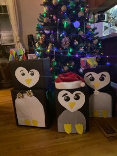 three penguins are sitting in front of a christmas tree