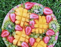 a platter filled with sliced up fruit on top of green grass next to watermelon and strawberries