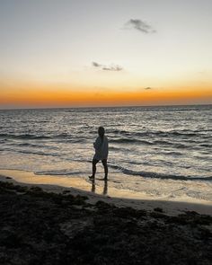 a man standing on top of a sandy beach next to the ocean at sun set