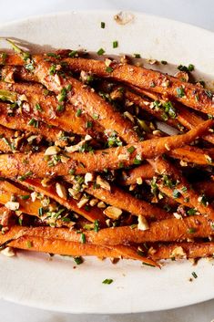 a white plate topped with sliced carrots covered in seasoning and chopped pine nuts