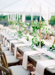 a long table with white linens and greenery is set up for an outdoor wedding