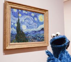 a blue sesame character standing in front of a painting on the wall with people looking at it