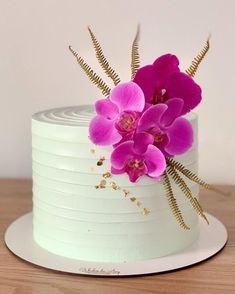 a white cake topped with pink flowers on top of a wooden table next to a wall