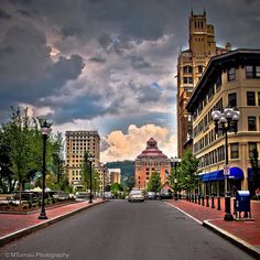 an empty street with cars parked on both sides and buildings in the background under a cloudy sky