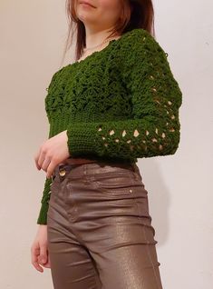 a woman is standing in front of a white wall wearing brown pants and a green sweater