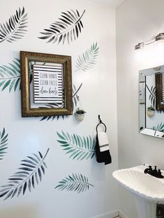 a bathroom with palm leaves painted on the wall and a mirror over the sink in front of it