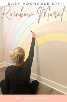 a woman sitting on the floor with her hand up in the air and writing, easy adorable diy rainbow mural