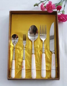 six forks, spoons and knives in a box on a table with pink flowers