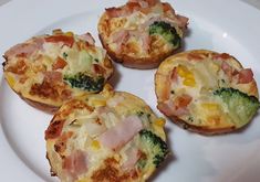 four small muffins on a white plate with ham and broccoli in them