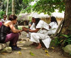 some people are sitting on the ground and one is handing something to another person with her hand