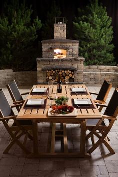 an outdoor dining table with chairs around it and a fire place in the back ground