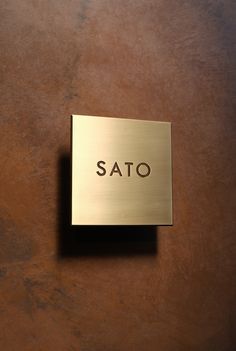 a metal sign that reads sato on it's side against a brown wall