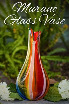 a colorful vase sitting on top of a wooden table next to white flowers and greenery