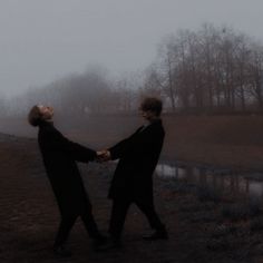 two people holding hands in front of a body of water on a foggy day