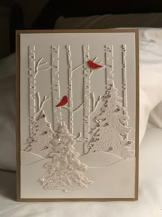 a white card with red birds sitting on top of trees and snow in the background