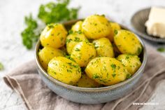 a bowl filled with yellow potatoes on top of a cloth next to butter and parsley