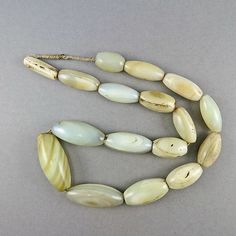 a long necklace with white and green beads on a gray surface, including one bead in the shape of an oval