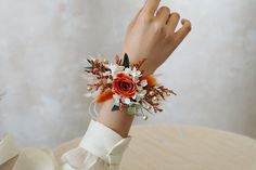 a wrist corsage with an orange rose, white and red flowers on it