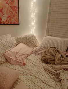 an unmade bed with blankets and pillows on top of it in front of a window