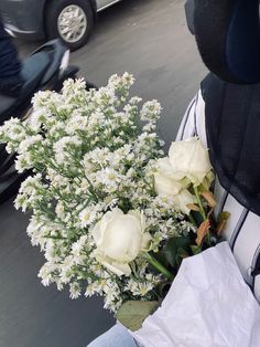 a bouquet of white flowers sitting on the back of a motorcycle parked in front of a car