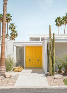 a yellow door sits in front of a white house with cactus and cacti