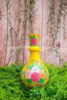 a yellow vase with flowers painted on it sitting in the grass next to a wooden fence