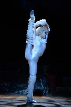 a woman in white performing on stage with her legs spread out and hands behind her head