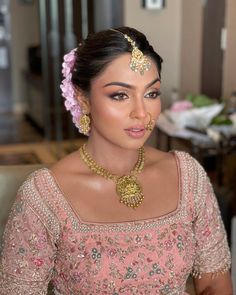 a woman wearing a pink outfit with gold jewelry on her head and in front of a mirror