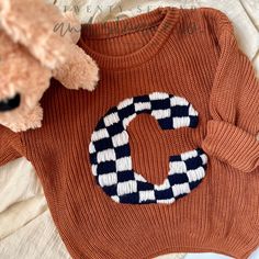 a teddy bear sitting next to an orange sweater with the letter c on it's chest