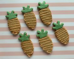 four cookies decorated like pineapples with green icing on a pink and white striped background