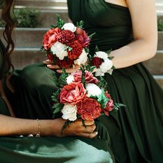 two bridesmaids in green dresses hold bouquets of red, white and pink flowers