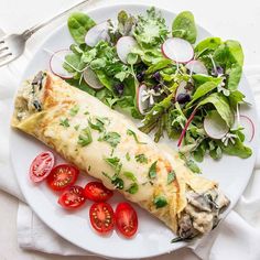 a white plate topped with an omelet next to a salad and a fork