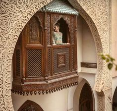 a woman standing on the balcony of a building with carved woodwork and stucco walls