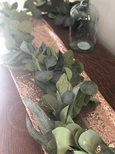 some green leaves are laying on a wooden table next to two glass bottles with water in them