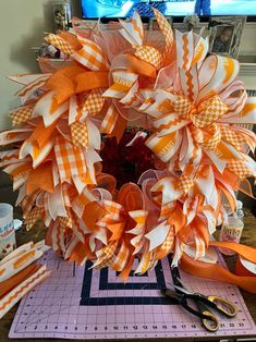 an orange and white wreath sitting on top of a table next to scissors, tape and other items