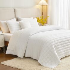 a bed with white comforters and pillows in a room next to a lamp on a table