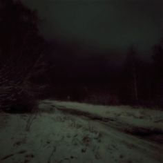 a snowy road in the woods at night with dark clouds and snow on the ground