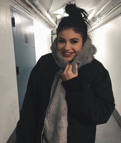 a woman is smiling while wearing a fur collar and scarf over her head in the hallway