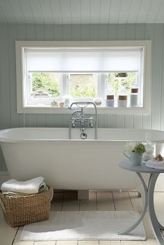 a white bath tub sitting under a window next to a table with towels on it