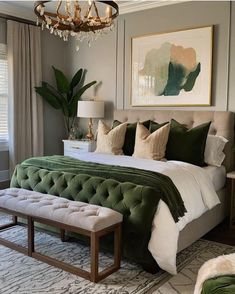 a bedroom with a large bed, green and white comforter, chandelier, two lamps, rugs and pictures on the wall