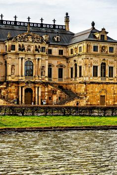 an old building sitting next to a body of water in front of a green field