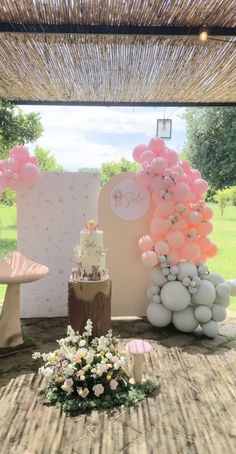 a table with balloons, cake and flowers on it in front of an outdoor area