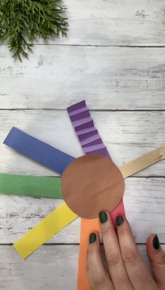 a person holding a piece of paper with different colored strips on it and a pine branch in the background