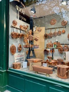 copper pots and pans are on display in the window of a storefront,