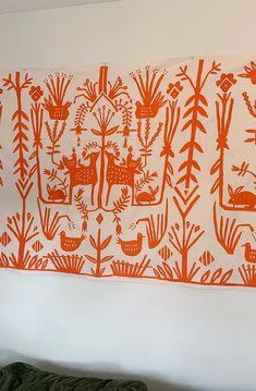 an orange and white wall hanging on the side of a bed in a room with plants